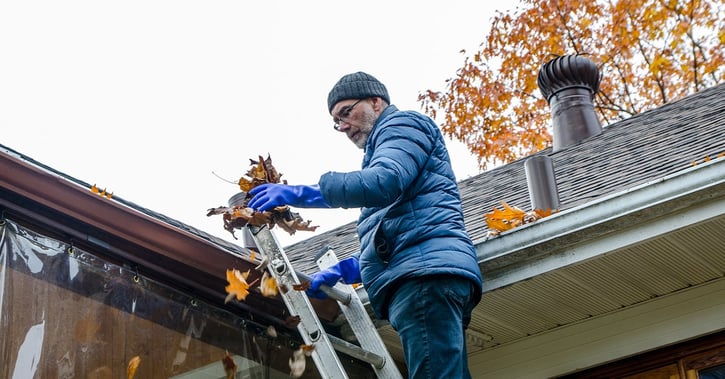 Man on ladder removing autumn leaves from gutter