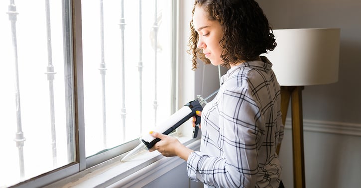 Woman caulking window at home